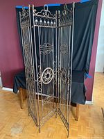Full view of the three-panel metal folding screen showing ornate framework and medallions.