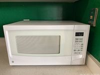 Front view of white GE microwave oven on countertop, showing windowed door and digital keypad.