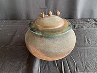 Full view of the round pottery jar with lid showing unglazed outer surface and three small bird figurines on lid.