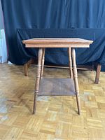 Front view of solid wood side table showing square top, four turned tapered legs and lower shelf