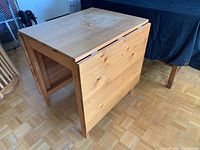Wooden drop leaf table folded showing natural wood finish and wear.