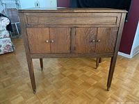 Front view of oak console showing hinged top panel, cabinet doors and tapered legs