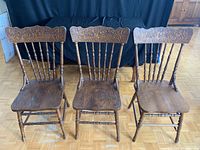 Three antique wooden chairs with carved detailed backrests and contoured seats, shown from front.