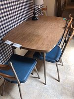Four vintage chairs with wooden backs, metal legs, and blue vinyl seats around a wooden table.