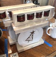Stacked boxed sets with one box of four white Christmas plates featuring a gold Christmas tree design and two boxes of four holiday-themed napkin rings with red background and gold reindeer/tree motifs, all sealed in original packaging.