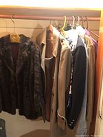 Wide view of hanging outerwear including fur coat, trench coat, blazer, jacket, and blouse