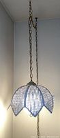 Photo showing the hanging light with the scalloped petal shaped shade lit up, suspended on a metal chain hanging from two ceiling hooks.