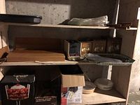 Shelf with broiler pan, serving trays, Black and Decker coffee maker, small ceramic dishes, and boxed kitchen appliances.