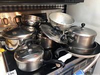 Multiple Farberware pots, pans and colander arranged on stovetop, showing set composition and condition with scratches.