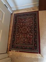 Full view of small rectangular rug showing red-based pattern and fringe on short sides.