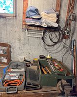 Overall view of the clamp-on vise, green toolbox with hand tools, socket set, and some clothing stored above on shelf.