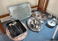 Overview of trays, serving dishes, baking dish, and utensils on floor near chair