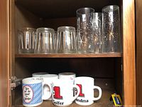 Wood cabinet shelf with six water glasses featuring starburst designs and six rocks glasses with vertical stripes.
