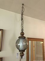 Hanging light fixture suspended from ceiling, featuring a large glass globe with swirled glass and brass decorative fittings, hanging chain included.