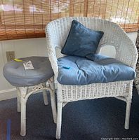 White wicker chair with blue cushion and blue throw pillow next to round wicker side table with gray cushion on top.