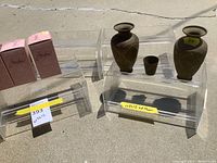 Overall view of four acrylic stands displaying two etched brass vases, one etched brass shot glass and three glass vases.
