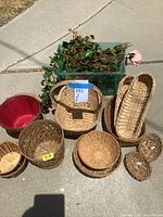 Overall view of assorted baskets and faux foliage arranged outdoors on pavement showcasing variety of basket shapes and materials.
