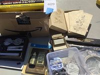 Box with office supplies and stationary, including compass, flashlight, label maker, various cords and accessories, embossed floral stationary cards.