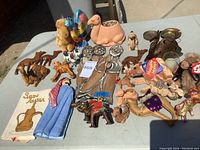Overview of assorted camel figurines and related decorative items on table including metal, plush, ceramic, and leather camels, Arabic style ashtrays, and textile items.