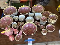 Overview of the full dishware set showing plates, bowls, teapot, spoons, and small vessels arranged on table.