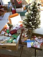 Overview of the lot showing the small decorated white Christmas tree and boxes filled with various Christmas ornaments