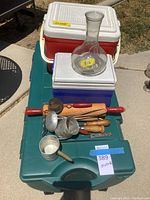 Photo of the two coolers, large storage trunk, glass decanter, and kitchen utensils arranged on the green trunk lid.