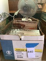 Photo showing net, fan, boxed Pocket Fisherman spin casting outfits and fishing line in cardboard box.