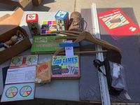 Photo showing assorted games including Parcheesi, Dominoes, Card Games, ceramic figurines, Avon treasure chest, a wooden hanger, shelving standards, and cardboard box.