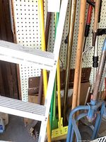 Photo showing assorted gardening tools with wooden handles, a blue dolly, and a metal step ladder.