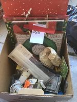 Box containing holiday gift bags and boxes, hot glue gun with glue sticks, a calculator, and wrapping items.