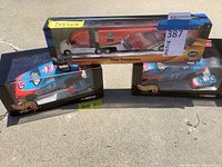 Three boxed Hot Wheels items displayed: a 2002 Hot Wheels Team Transport truck with car in original packaging, and two Hot Wheels Racing NASCAR large cars with small matching cars in boxes.
