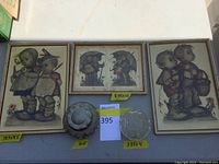 Three framed Hummel reproduction prints and two glass candy dishes displayed on a surface. Prints display children in period clothing, glass dishes are clear and one has a chipped lid.