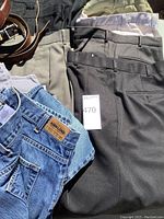 Lot showing men's casual pants and jeans with three leather belts; pants include Haggar, Claiborne, Motion, and Kirkland brands.