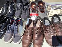 Photo showing various men's shoes including leather dress shoes, black sneakers, gray running shoes, navy casual sneakers, and brown leather shoes with shoe horn.