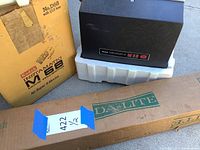 Image shows Kodak Instamatic M68 projector in black with original box labeled No. D68 with 1/15 lens for Super 8 movies, alongside a long rectangular cardboard box labeled Da-Lite.