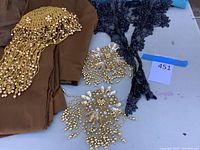 Photo showing the brown fabric with gold beaded headdress and gold sequin bead decorative collar pieces laid out on a surface with a black lace applique.
