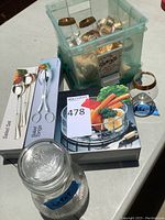 Full set of serveware items arranged outside a plastic translucent bin, showing the snifters, salad tongs, napkin rings, crystal bowl, and Hidden Valley dressing jar.