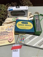 Photo showing the boxed Sonorous portable wireless speaker, book, glass pens, calculator, and decorative heart-shaped lock on display.