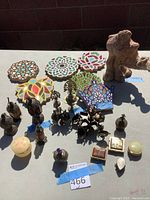 Photo of colorful floral and geometric decorative tiles, ceramic camel figurine, ornamental perfume bottles, and small boxes arranged on table surface in daylight.