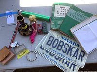 Photo of various items including license plates, books, a small figurine, decorative vase, and stationary on a table.