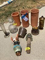 Photo showing three terra cotta wine coolers, glass carafe, dark ceramic pots, pepper grinder, decorative scarecrow figure, wooden handled glass item