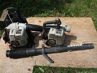 Two used Echo backpack leaf blowers laid on wood, each with attached blower tubes; clear view of overall items for sale.
