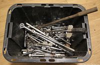 Plastic bin filled with various ratchet tools including ratchets, extension bars, and handles placed on wooden floor