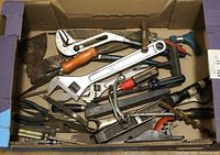 Box containing assortment of used hand tools including wrenches, screwdrivers, pliers, files, hand saw parts and an axe head.