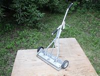 Photo of the front and handle of the magnetic sweeper placed on plywood outdoors showing overall condition and size.
