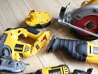 Overhead view of jigsaw, cordless battery, circular saw blade and reciprocating saw on wood floor