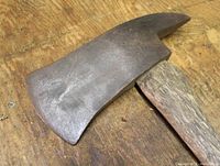 Close-up photo of the metal axe head showing the broad blade and pointed pick, resting on a wooden surface.