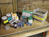 Overview of assorted containers and boxes of various screws and hardware on a wooden surface.