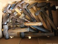 Box of assorted used hatchets, hammers and mallets showing various handle and head types and wear.