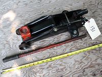 Used black hydraulic car jack with red lifting saddle and mismatched red handle next to a tape measure showing approximate length of handle